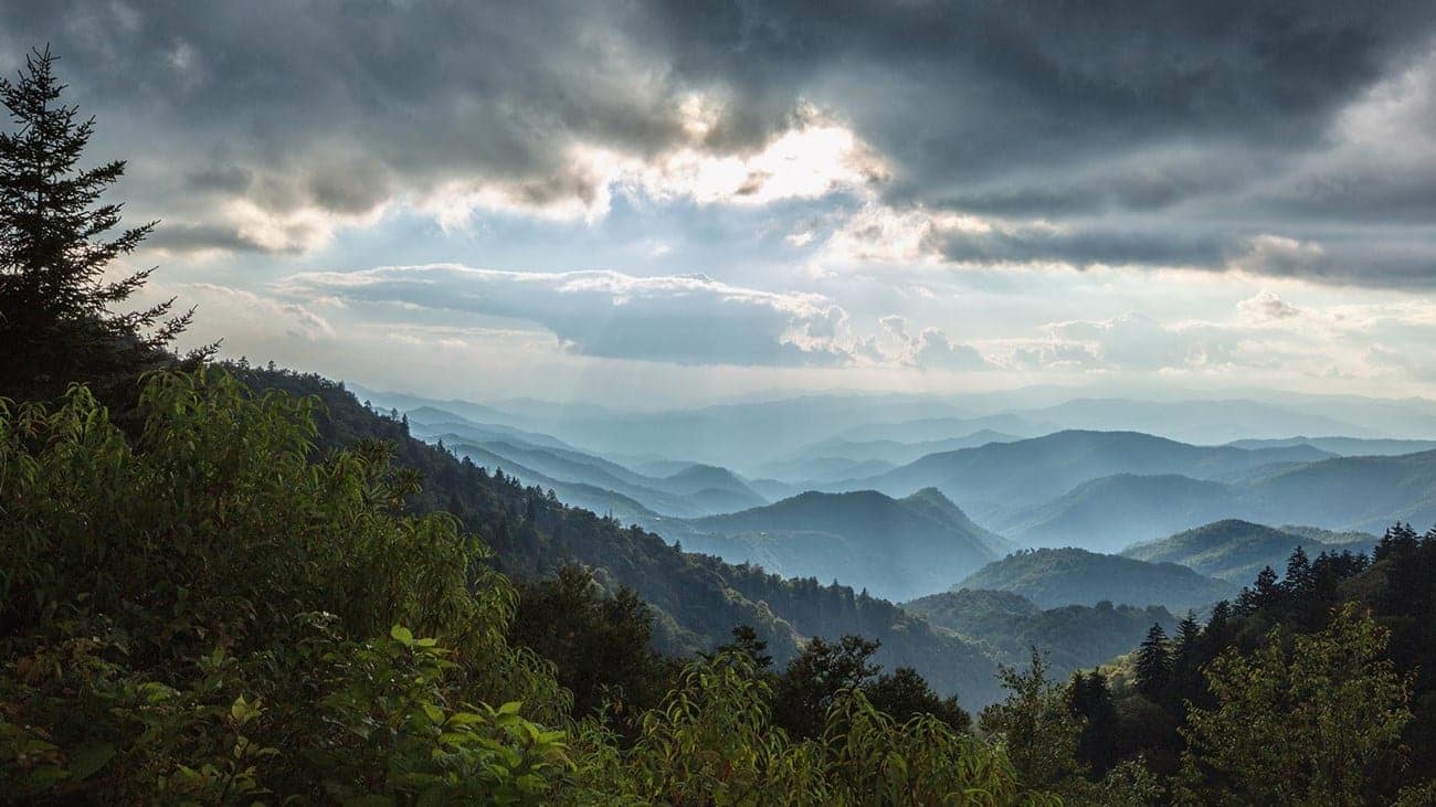 Panoramic view of layered mountain ridges under a dramatic sky with sunbeams piercing through clouds, labeled as Auto Draft.