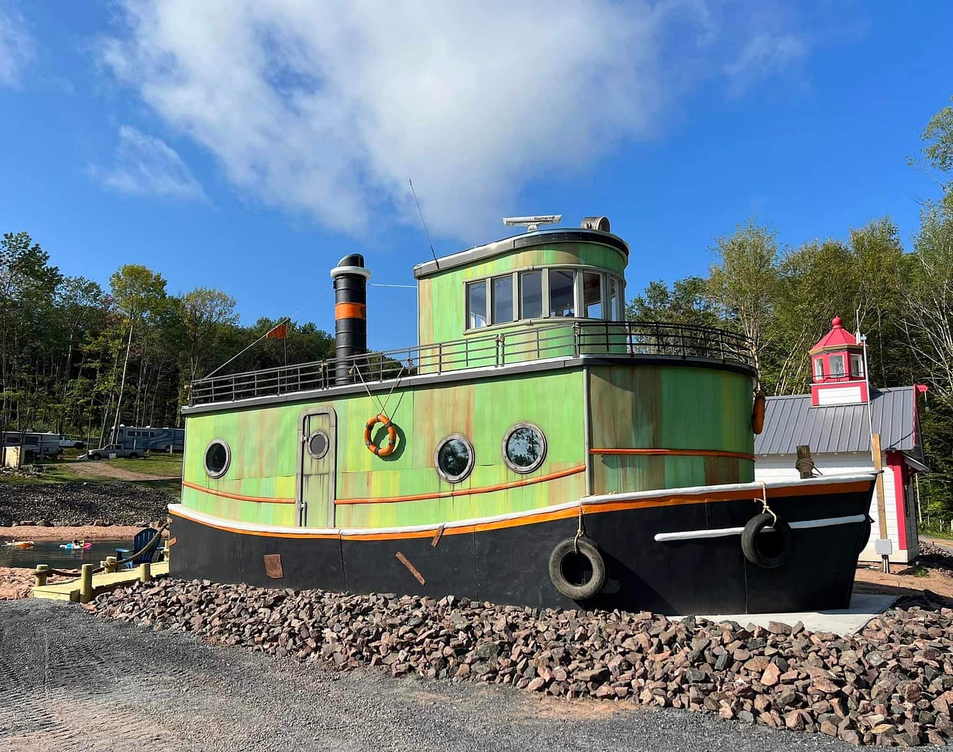 A green and black tug boat, exuding an aura of adventure, is parked in front of majestic rocks at the Apostle Islands Campground.
