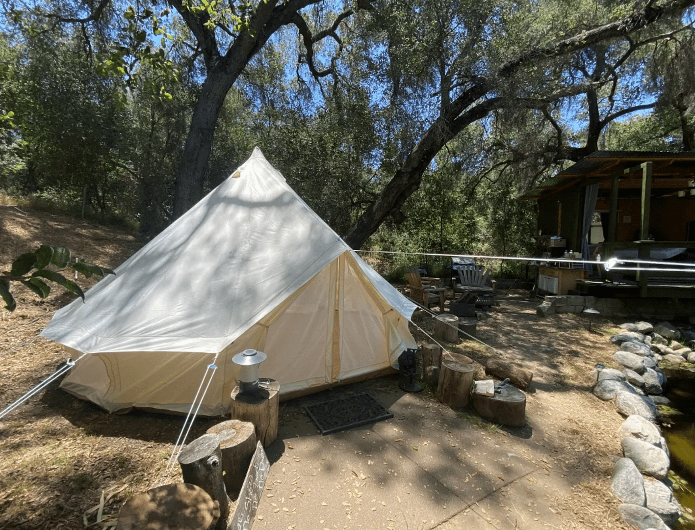 A white glamping tent sits next to a tree in a wooded area, belonging to private property owners.