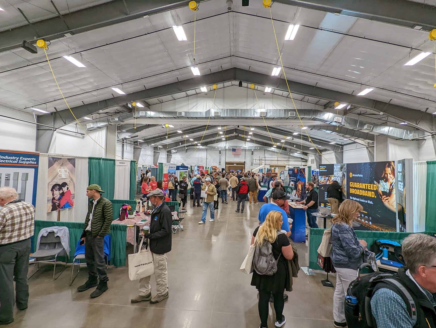 Whitney Scott delivering a keynote presentation at The Glamping Show USA, with a group of people walking around in a large building.