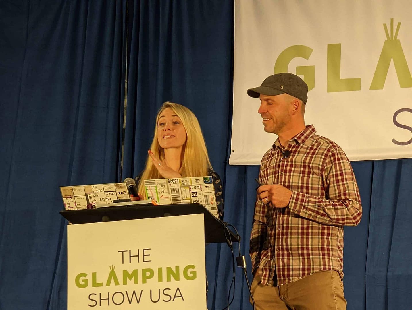 Two individuals, a man and woman, confidently standing at a podium during the Glamping Show USA.
