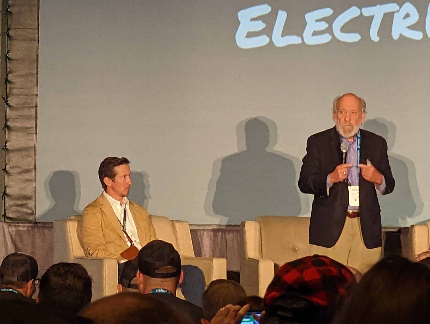 An expert is speaking on stage at a conference about the future of electric cars.
