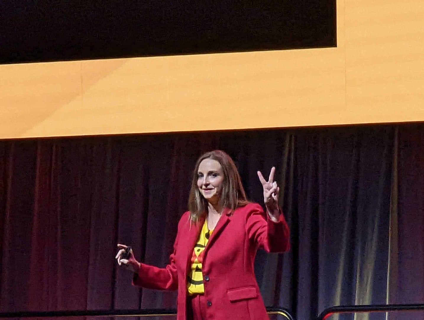 A woman in a red suit giving a speech at a convention.