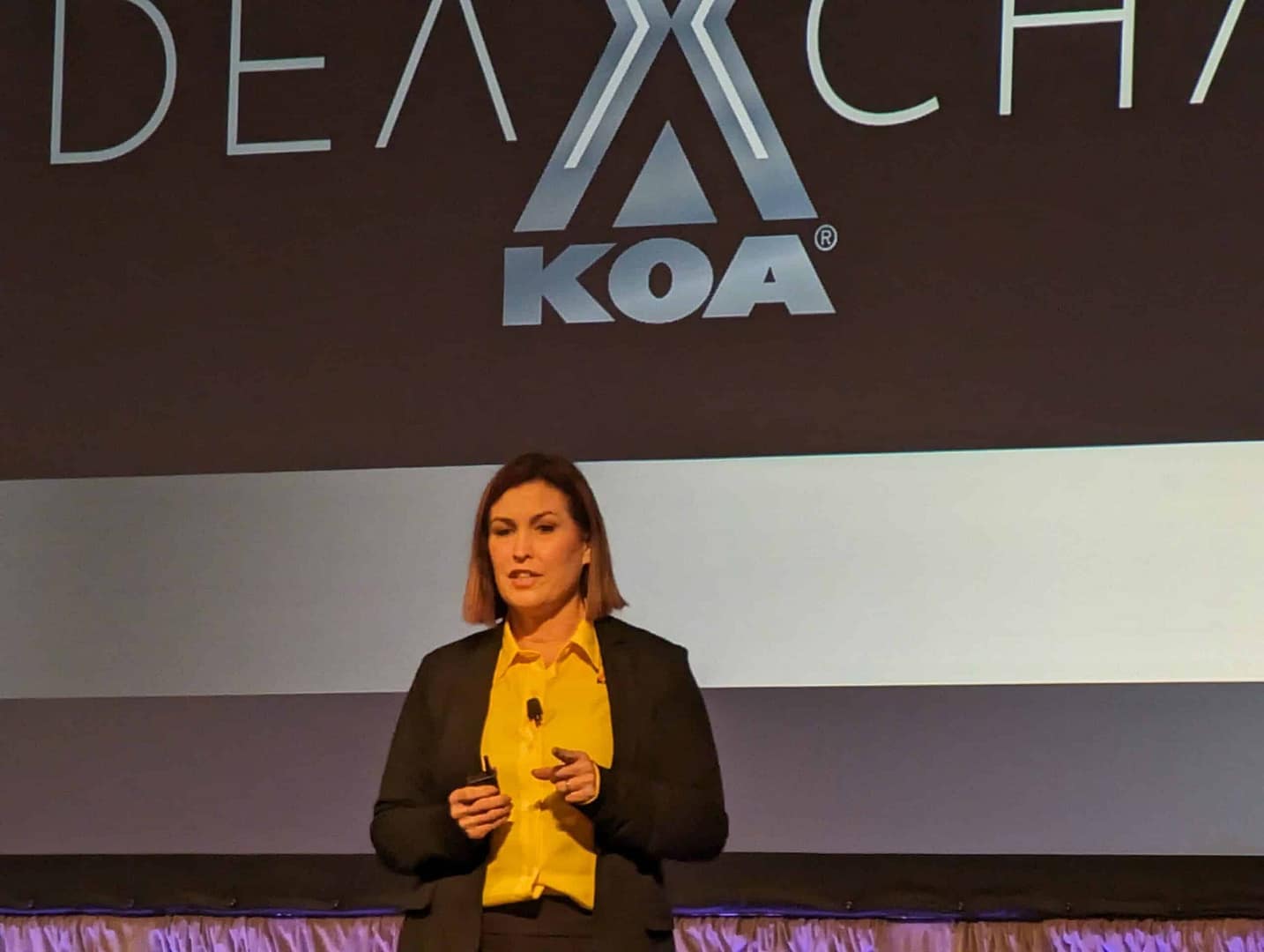 A woman standing in front of a screen with the words IdeaXchange KOA.