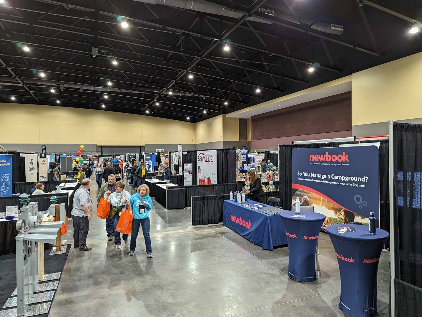 A large convention hall with people networking around booths at the Campground Owners Expo.