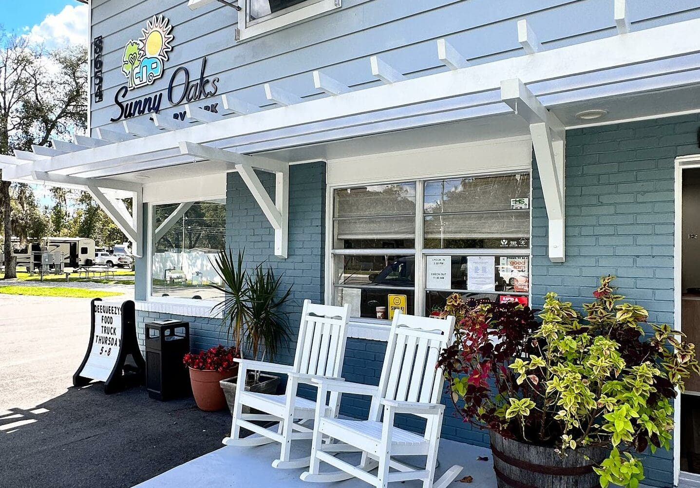 A sunny day at the front of Sunny Oaks RV Park with two white rocking chairs.