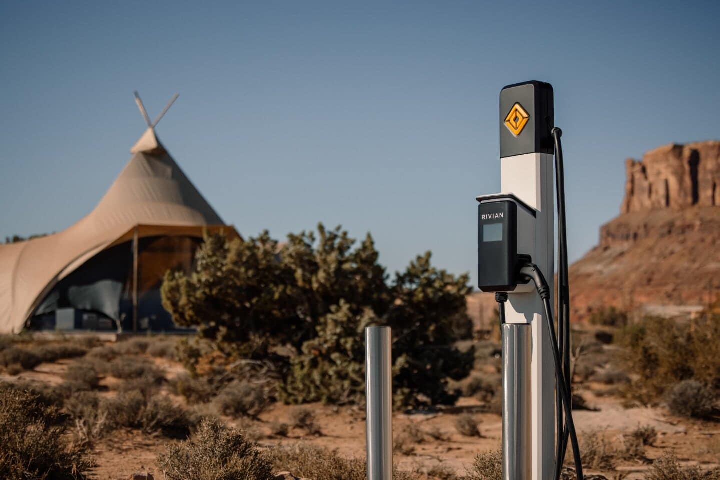 A Rivian charging station in the desert with a teepee in the background.