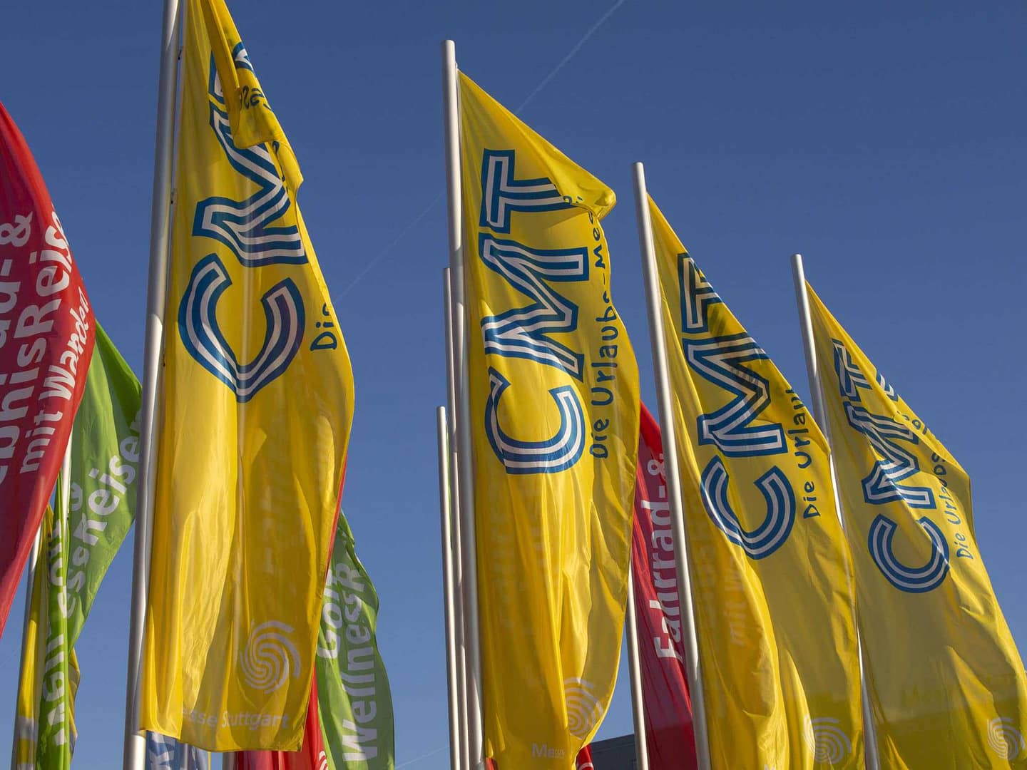 A group of flags in front of a blue sky at the Trade Fair Ban.