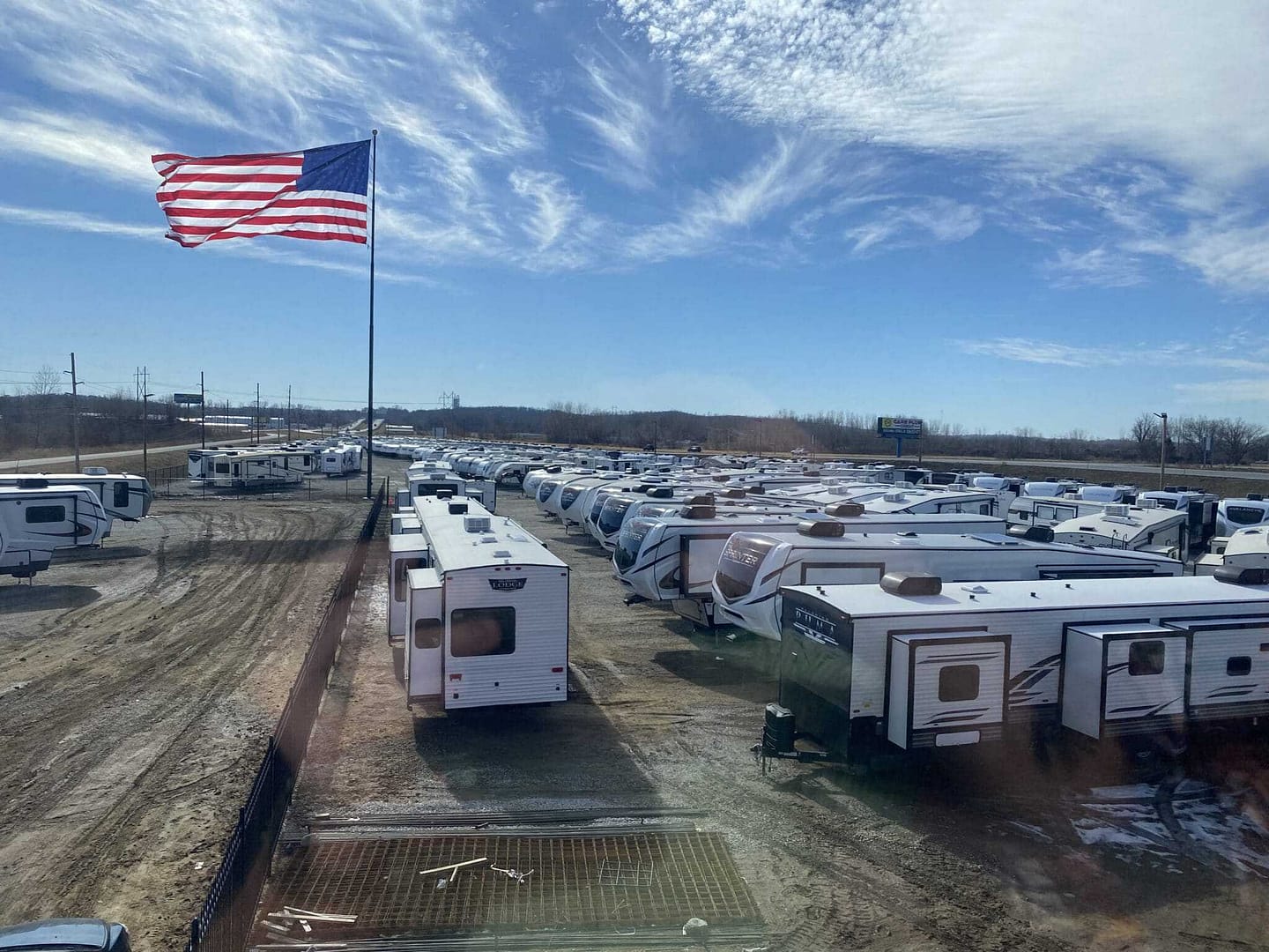 Many RVs parked at an Unlimited RV dealership in Missouri with an American flag.