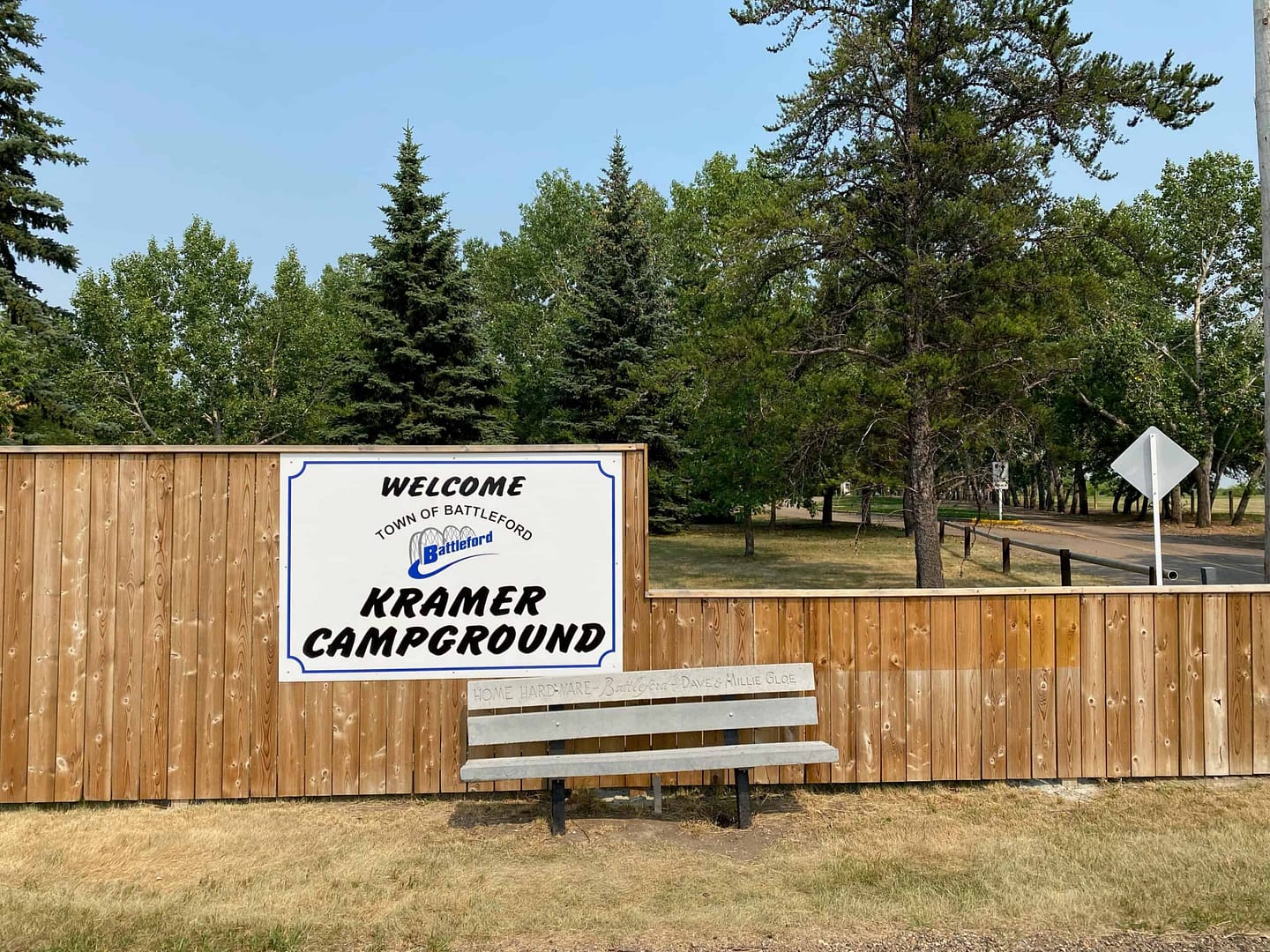 A wooden bench sits in front of a sign that says welcome to Eiling Kramer Campground, during the busy camping season.