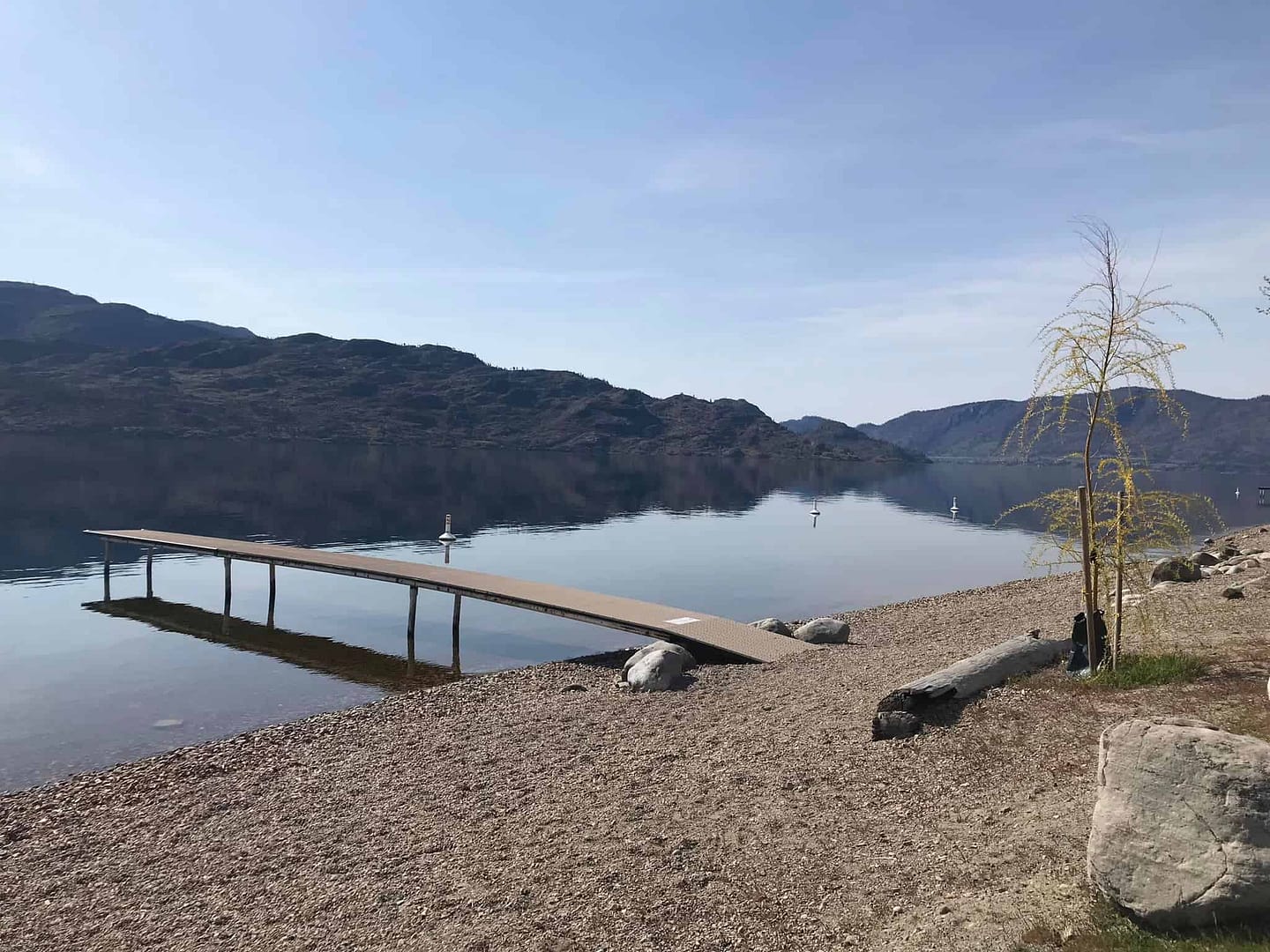 A dock on the shore of a lake with mountains in the background, located in Peachland.
