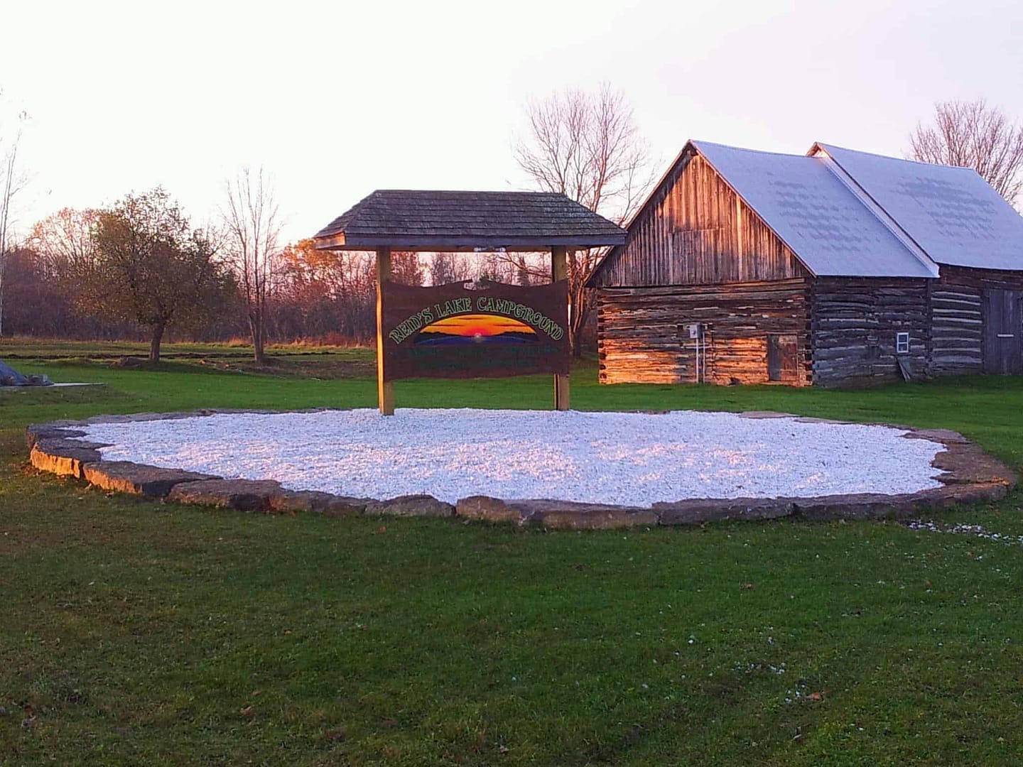 A sign in front of Reid's Lake Campground barn with a rainbow in the background.