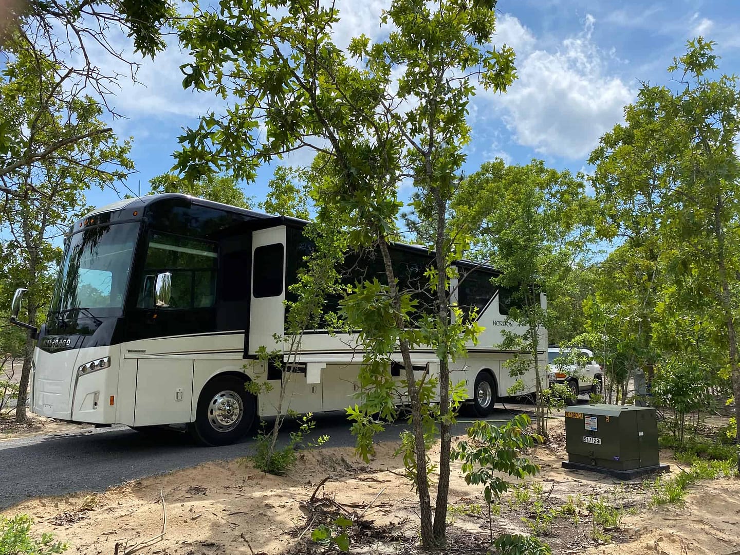 A white RV parked in a wooded area at an RV resort.