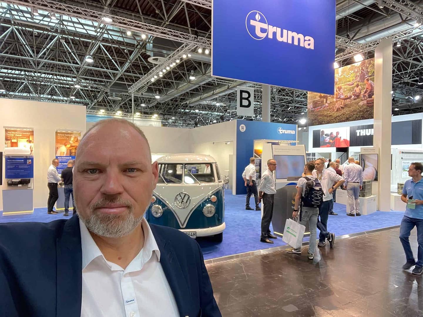 A man in a suit is taking a selfie at CARAVAN SALON Düsseldorf, a trade show for minivan conversions.