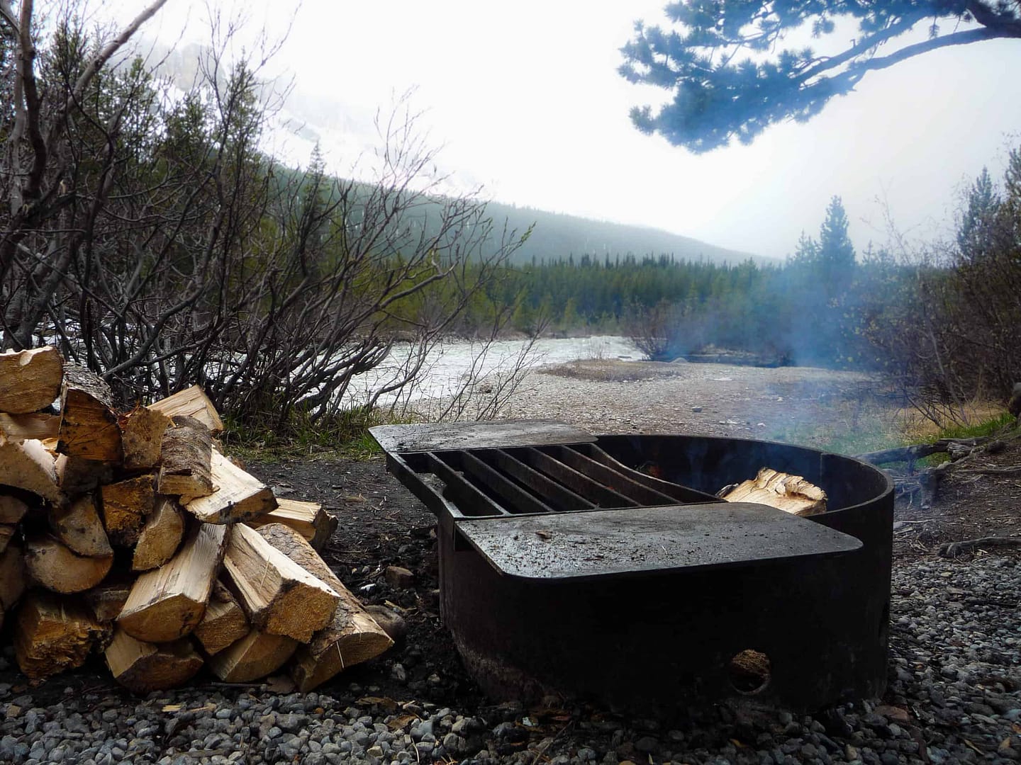 An Expand fire pit with logs on it next to a river at Rowan's Ravine Provincial Park.