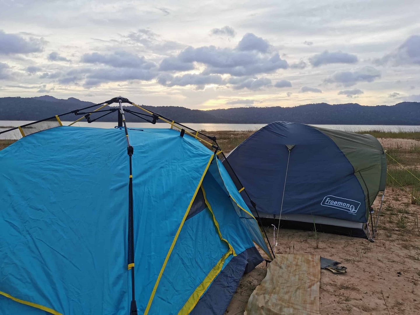 Two tents set up on the sand next to a body of water in Selangor, an unregistered camping ground.