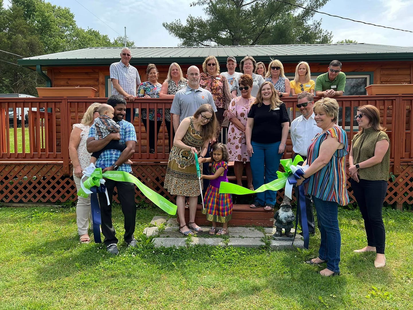 A group of people cutting a ribbon in front of the LazyLlama Campground cabin in Greene County, with family-friendly amenities.