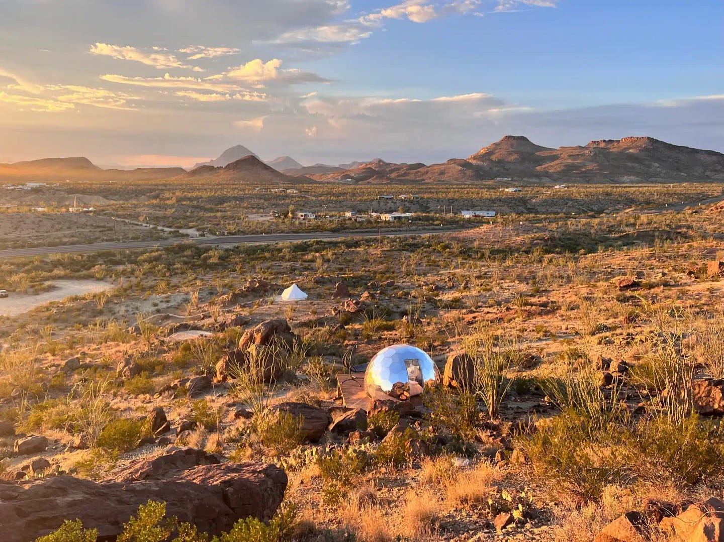 A glass dome in the desert with mountains in the background, perfect for an unforgettable glamping experience in the U.S.