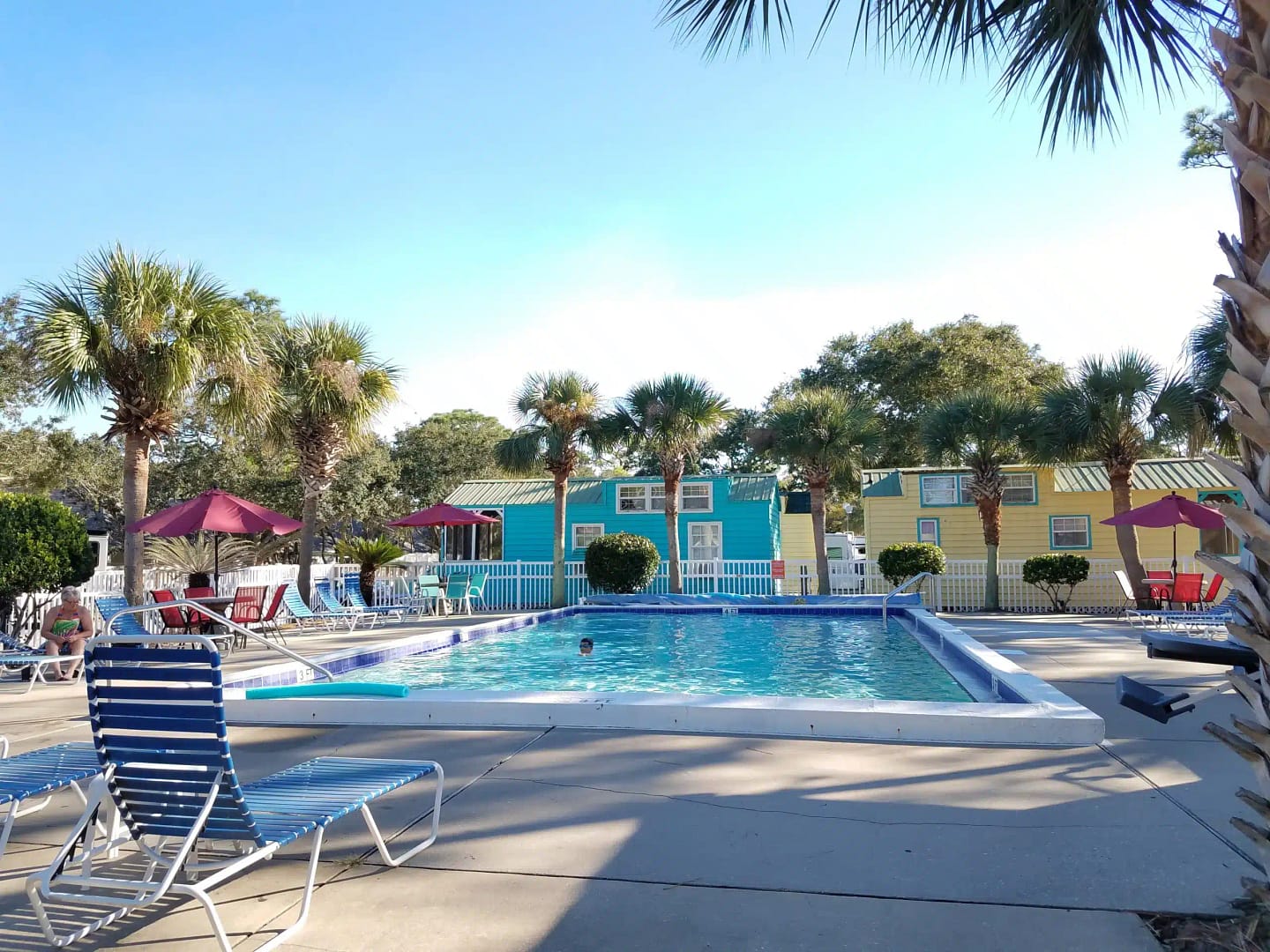 The Navarre Beach Camping Resort offers a delightful swimming pool oasis with lounge chairs and palm trees, perfect for snowbirds and winter guests seeking relaxation.