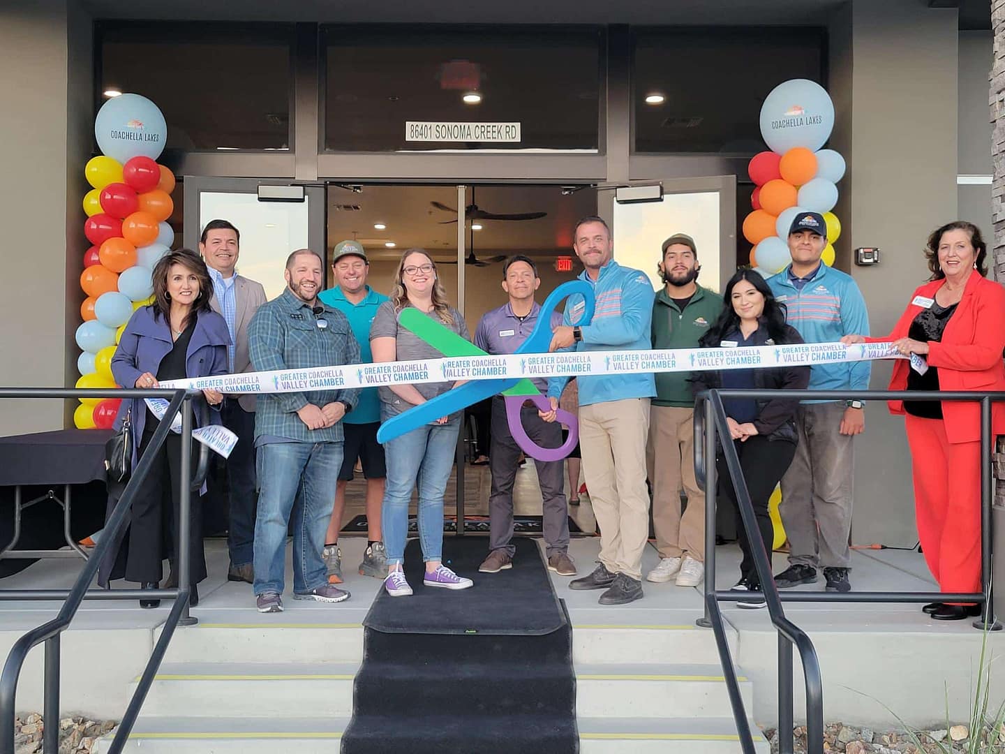 A group of people standing in front of a building with a ribbon for the Grand Opening of Coachella Lakes RV Resort.