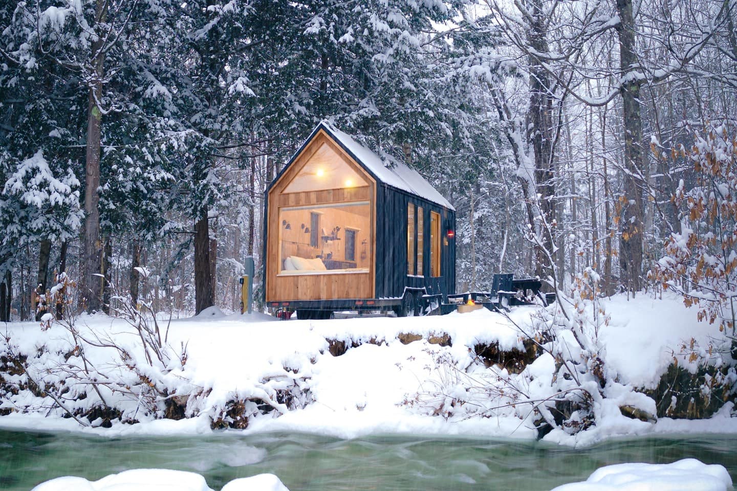 A tiny house in the woods with snow on the ground at New England's Lumen Nature Retreat.