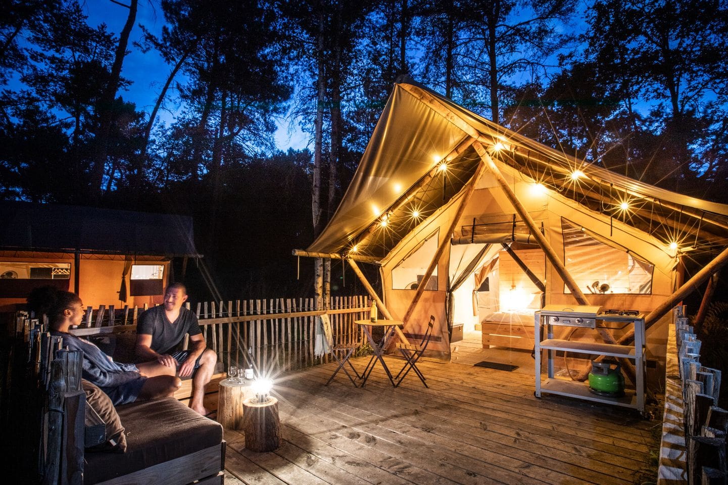 Two people sitting on the deck of a Solar-Powered hut in the woods.