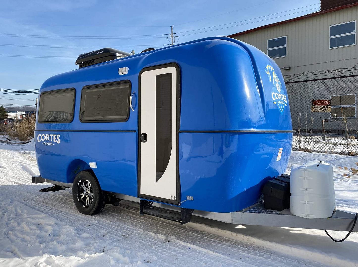 A blue camper trailer from Cortes Campers is parked in the snow.