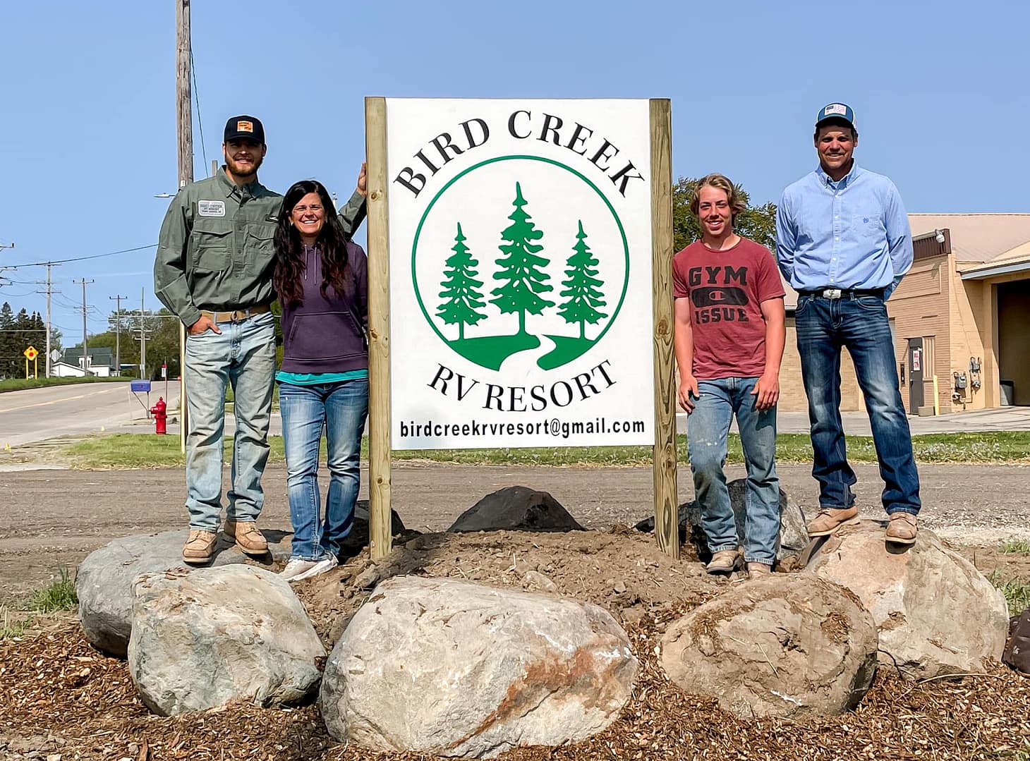 A group of people standing in front of a sign that says Bird Creek RV Resort.