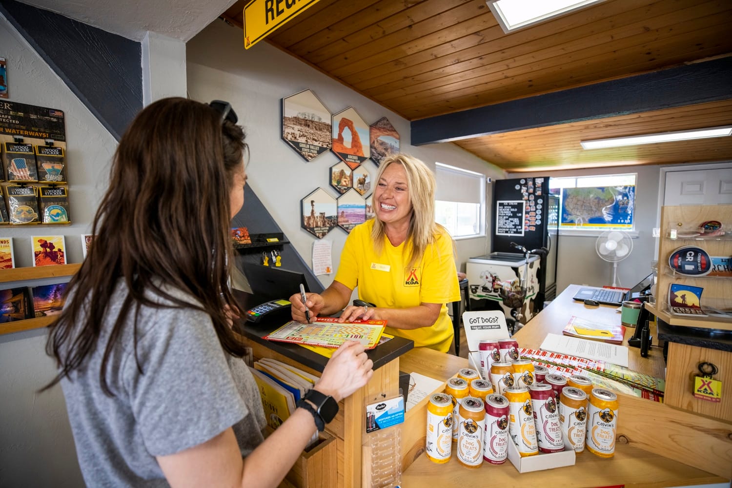 A woman in a yellow shirt is standing at the counter of KCN Campgrounds, an outdoor hospitality industry store.