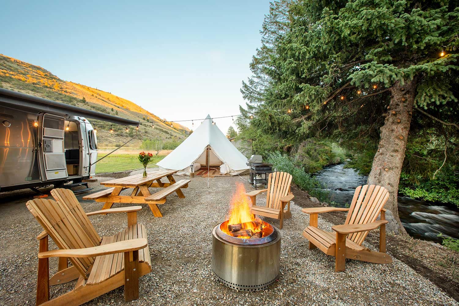 A teepee nestled in a wooded area with a fire pit in the middle, offering limited-time discounts and possible upgrades. Welcome to Moose Creek Ranch!