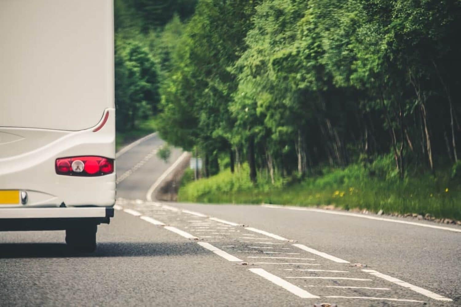 A white bus driving down a country road near William's Den, promoting road safety.