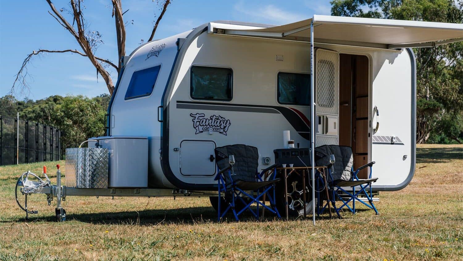 A Mystic 12 Travel Trailer parked on a grassy field with chairs set up outside under an awning, revolutionizing affordable RV living.