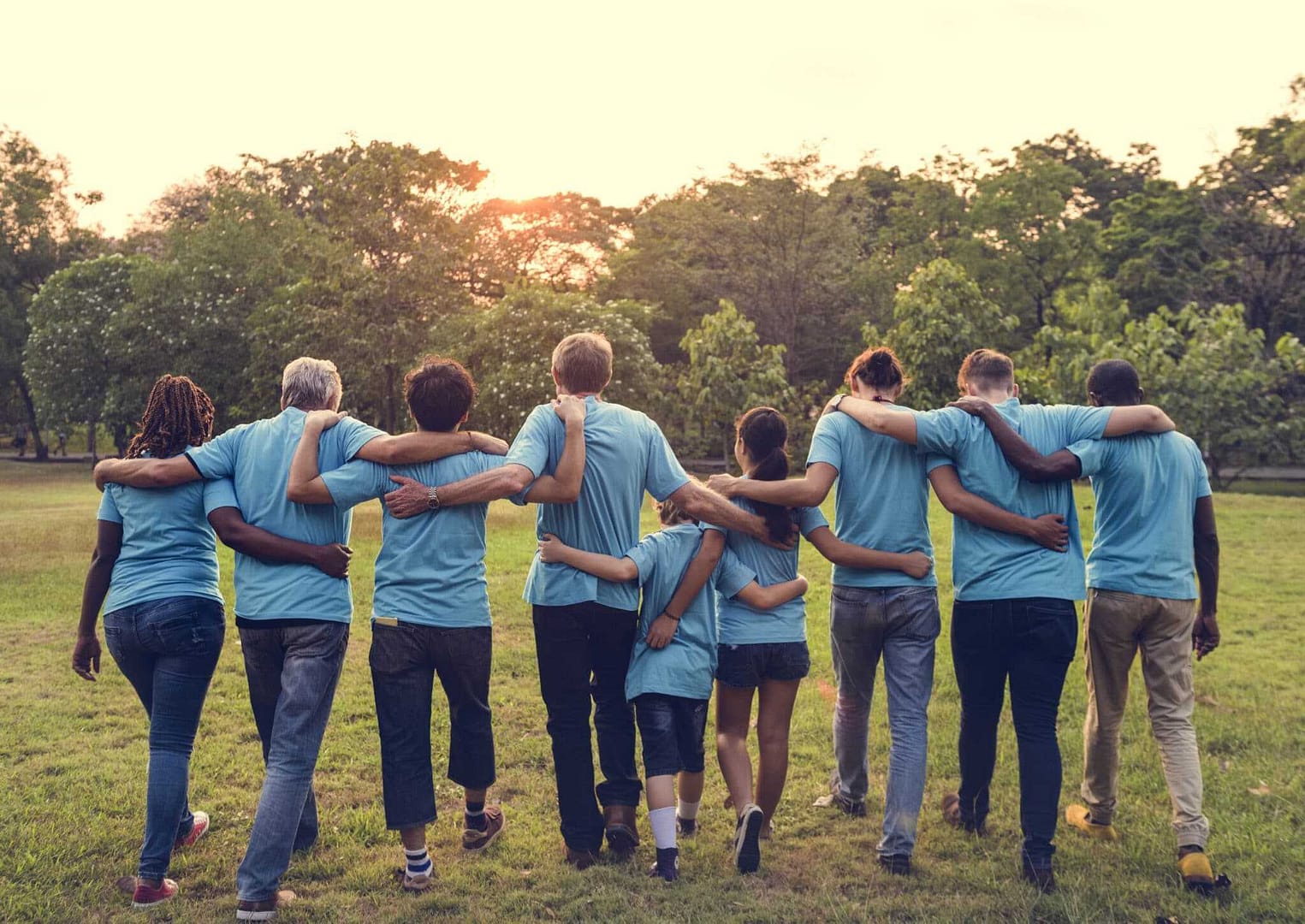 A group of Volunteer Hosts in blue shirts standing together in a park near the Pocatello Field Office of BLM.