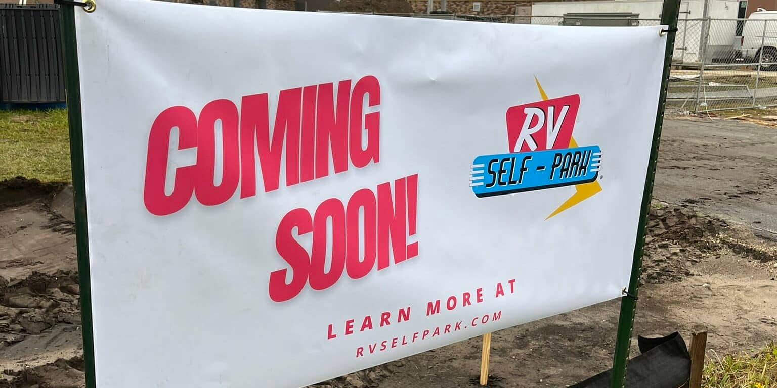 An automated sign that says coming soon is in front of a construction site for an RV self-park.