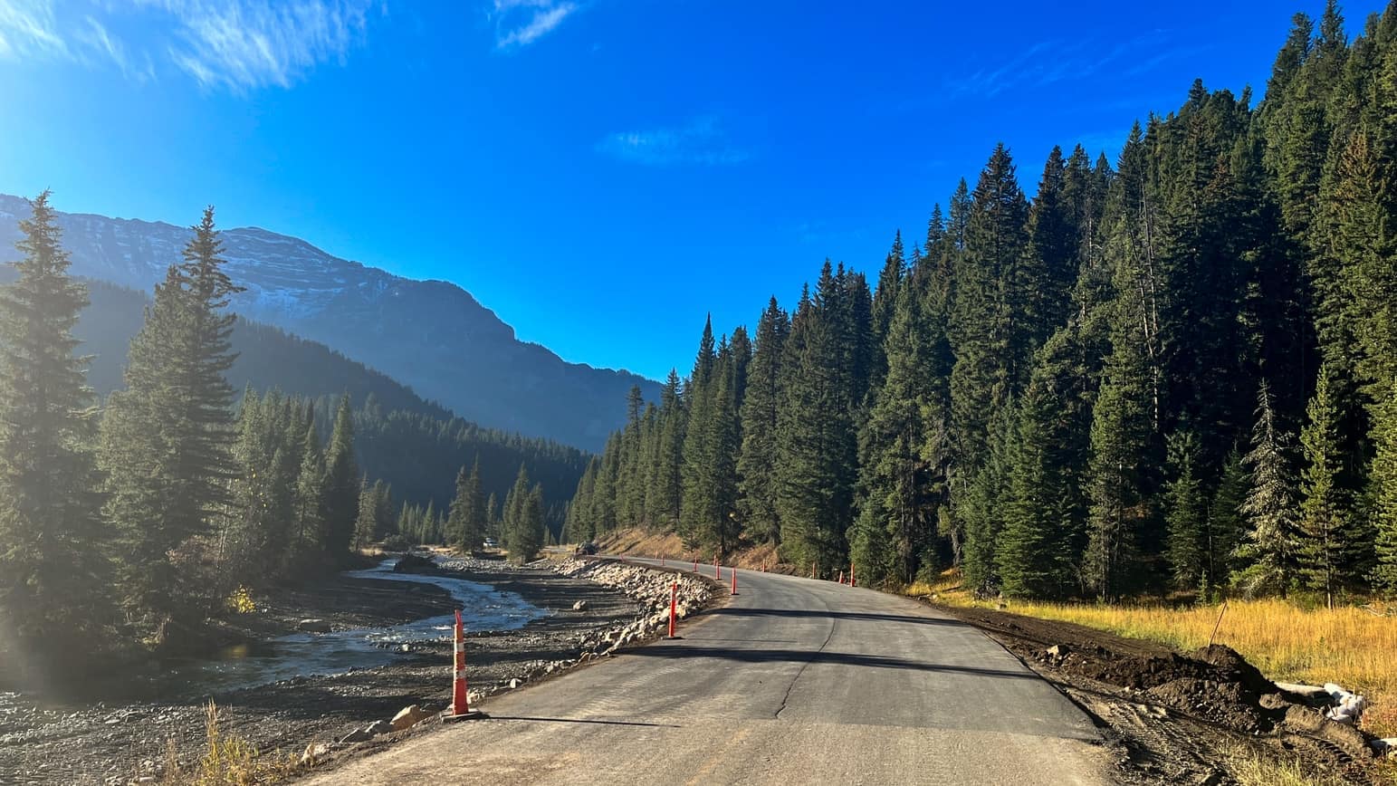 A road near the entrance of Yellowstone National Park winds through the majestic mountains while hugging the serene river, offering enchanting views to visitors.