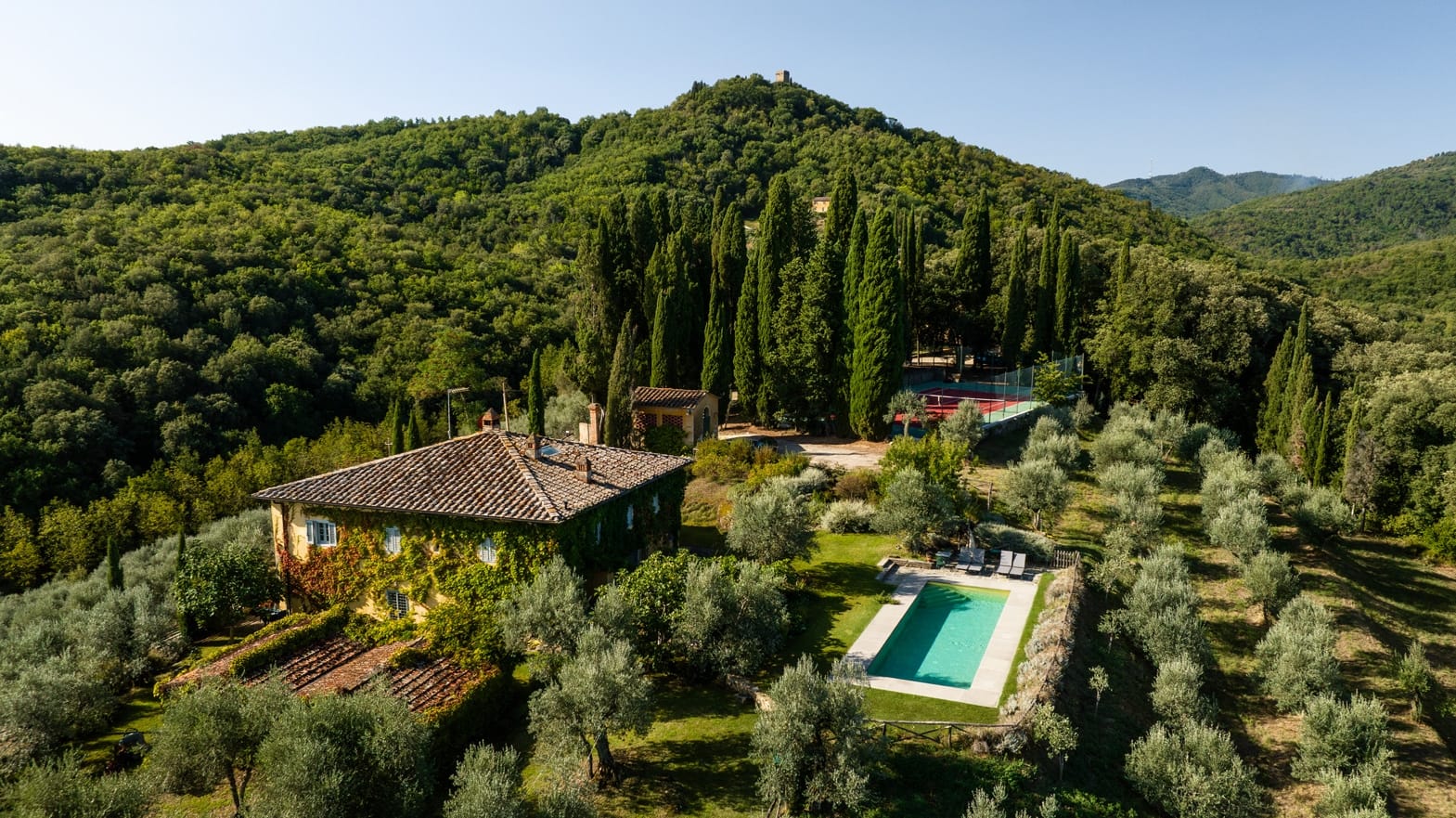 Aerial view of a rural villa with a swimming pool surrounded by lush greenery and cypress trees, Auto Draft.