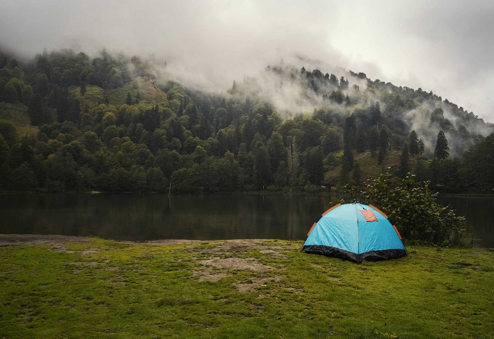 A blue tent sits on the grass next to a lake at a campground in Maine.