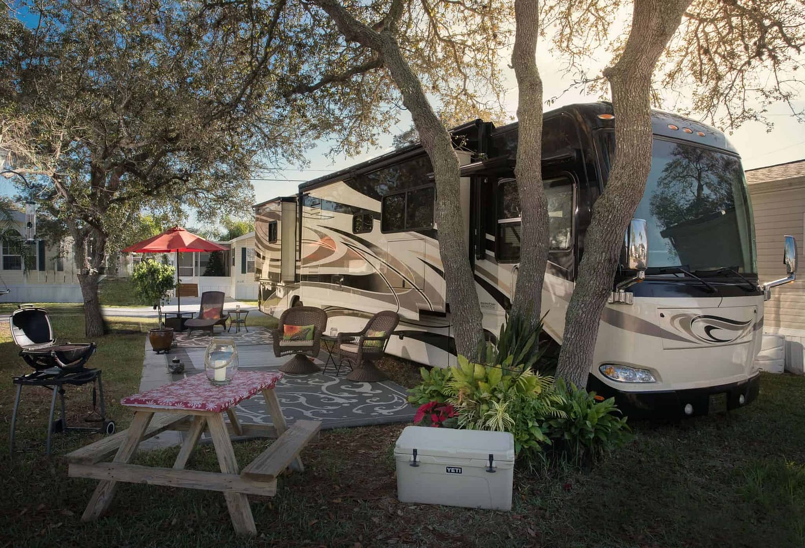 A newly sold RV, now under new management, is parked in a yard with a table and chairs.