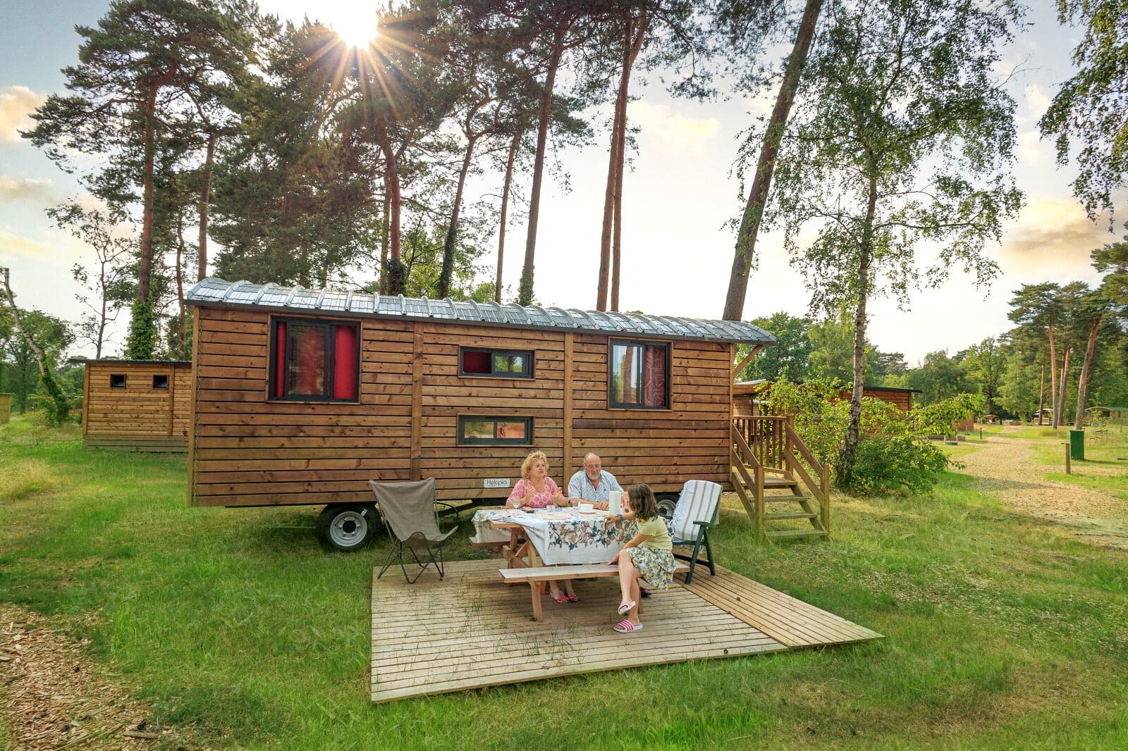 Hekipia, a French Tiny House Specialist, launches their U.S. factory with two people sitting at a table in front of a tiny house.