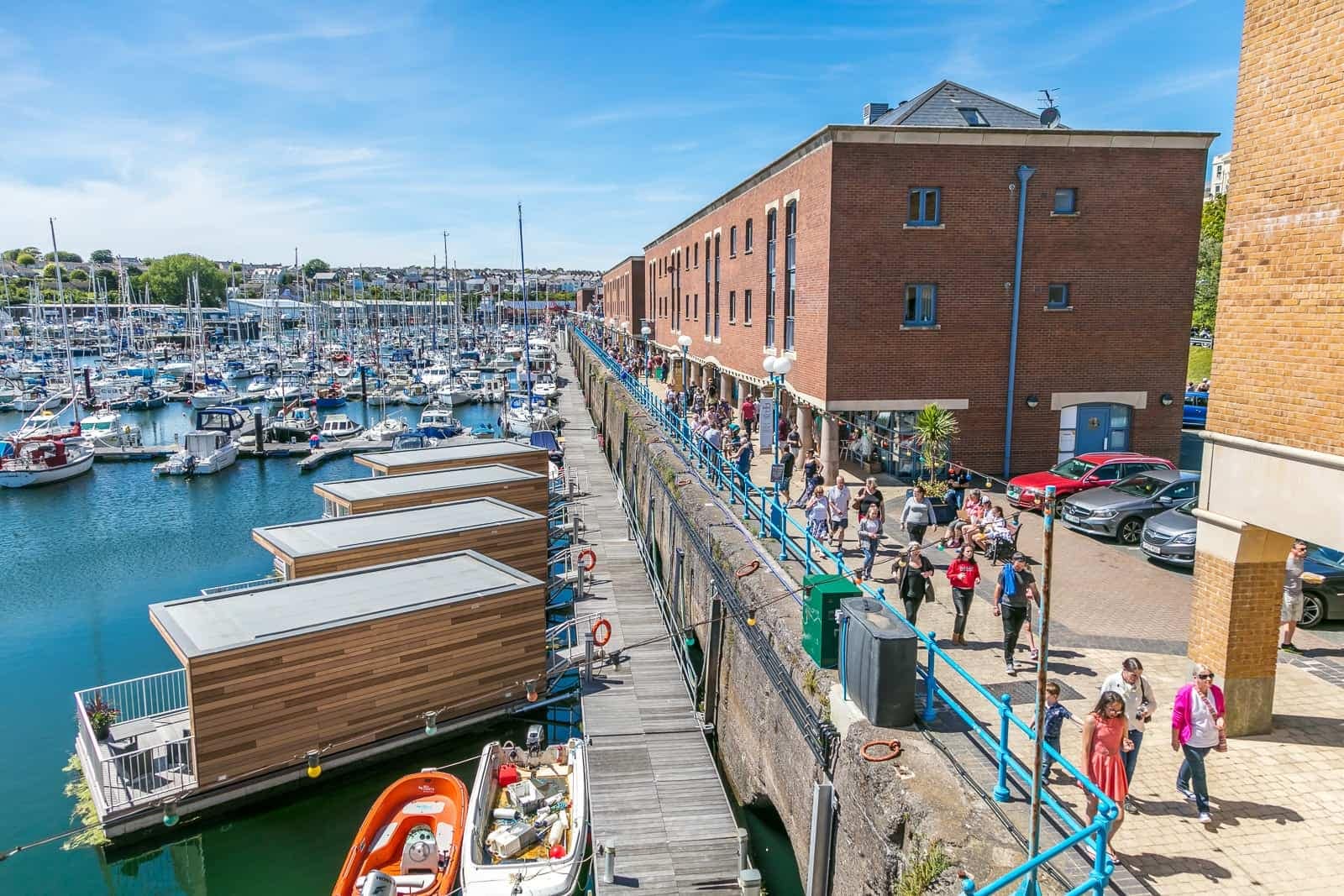 People walk along a unique dock with floating boats in the background at Milford Haven.