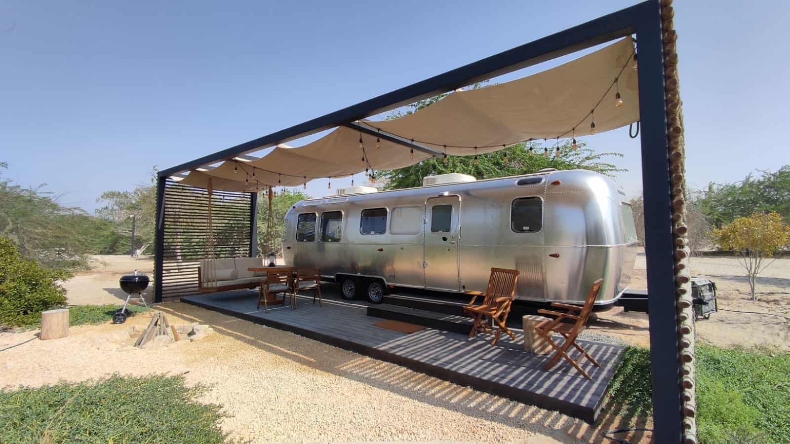 A silver airstream trailer is parked under a canopy, offering a unique glamping experience in the UAE.