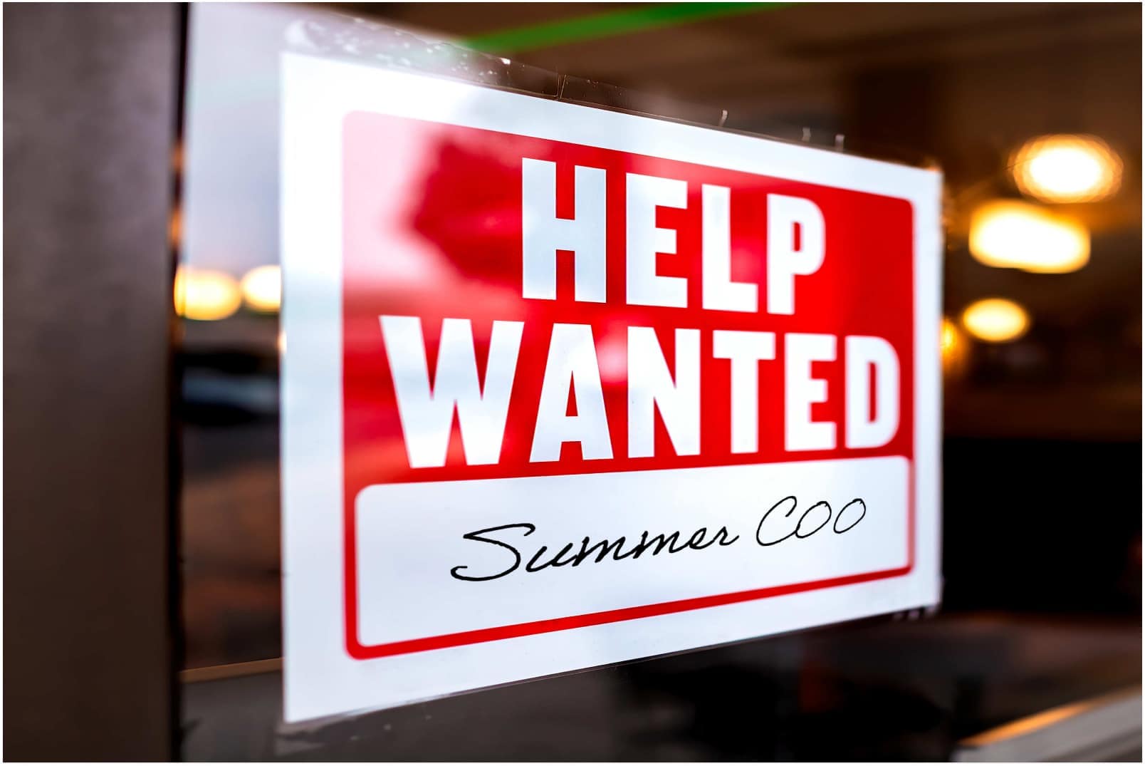 A sign that says help wanted summer cook hangs in a restaurant.