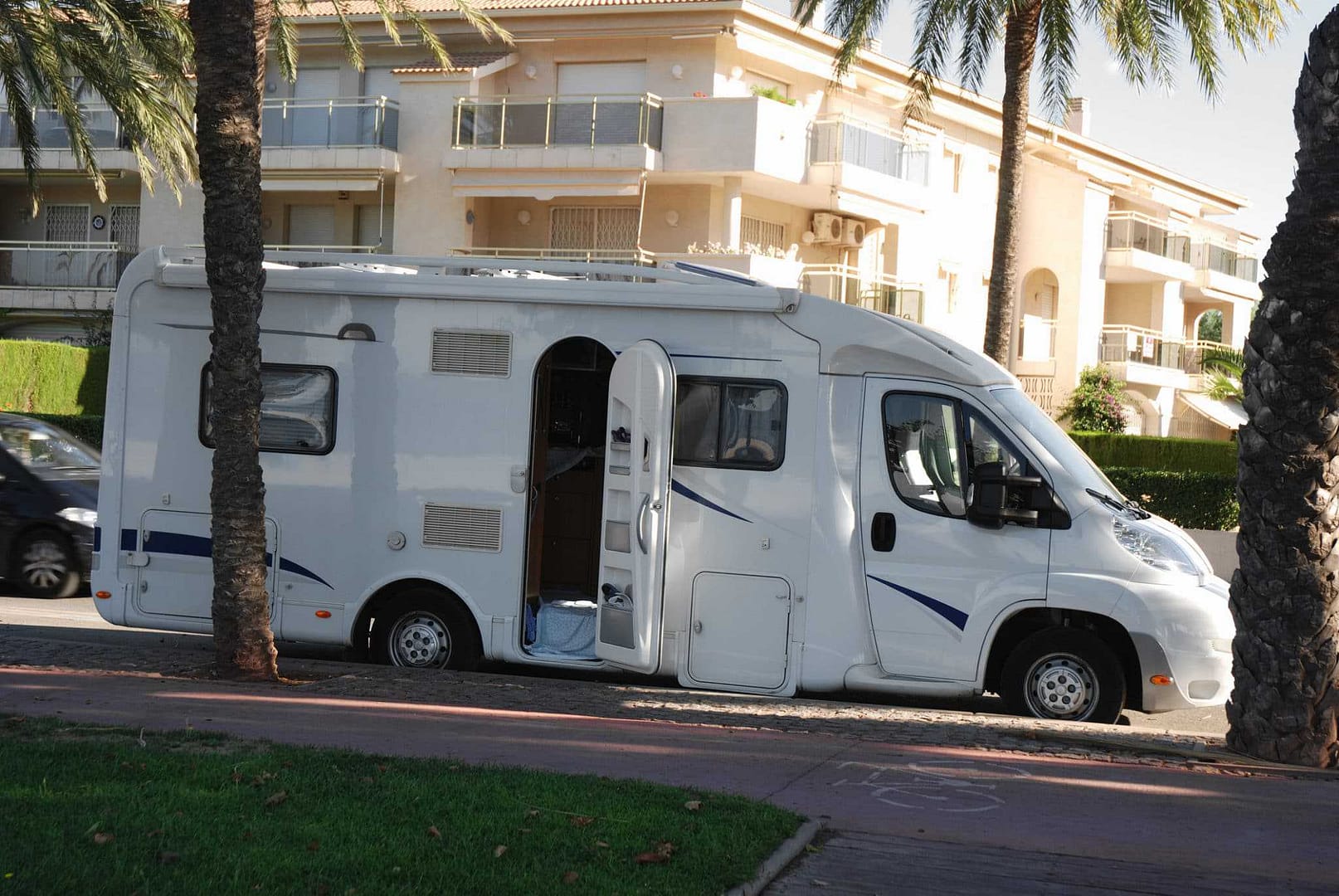 A white RV parked next to a palm tree in an Alberta town, despite the town council's strict RV parking restrictions that could result in fines.