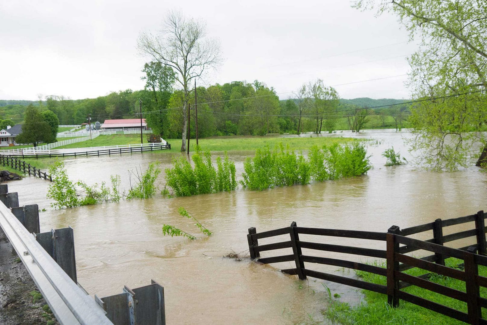 A flooded road in Middle Tennessee with a fence and farm in the background.