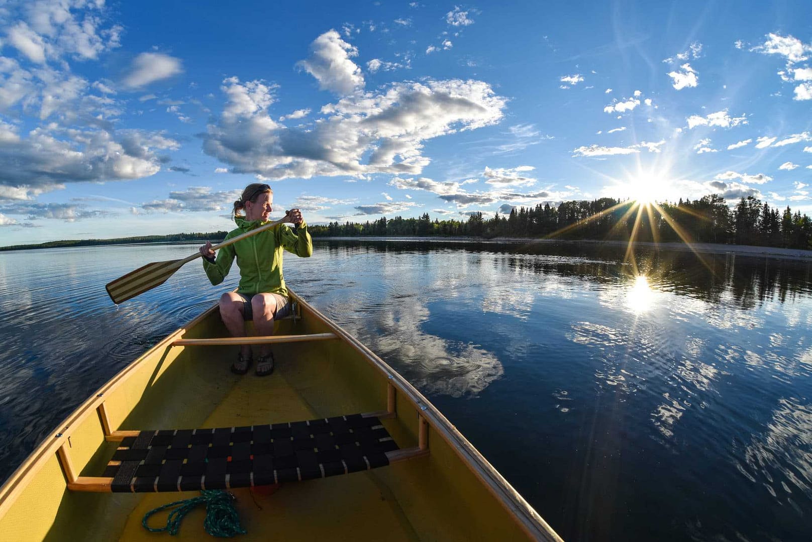 A woman paddles a canoe on a lake in Saskatchewan, enjoying the serene natural infrastructure.