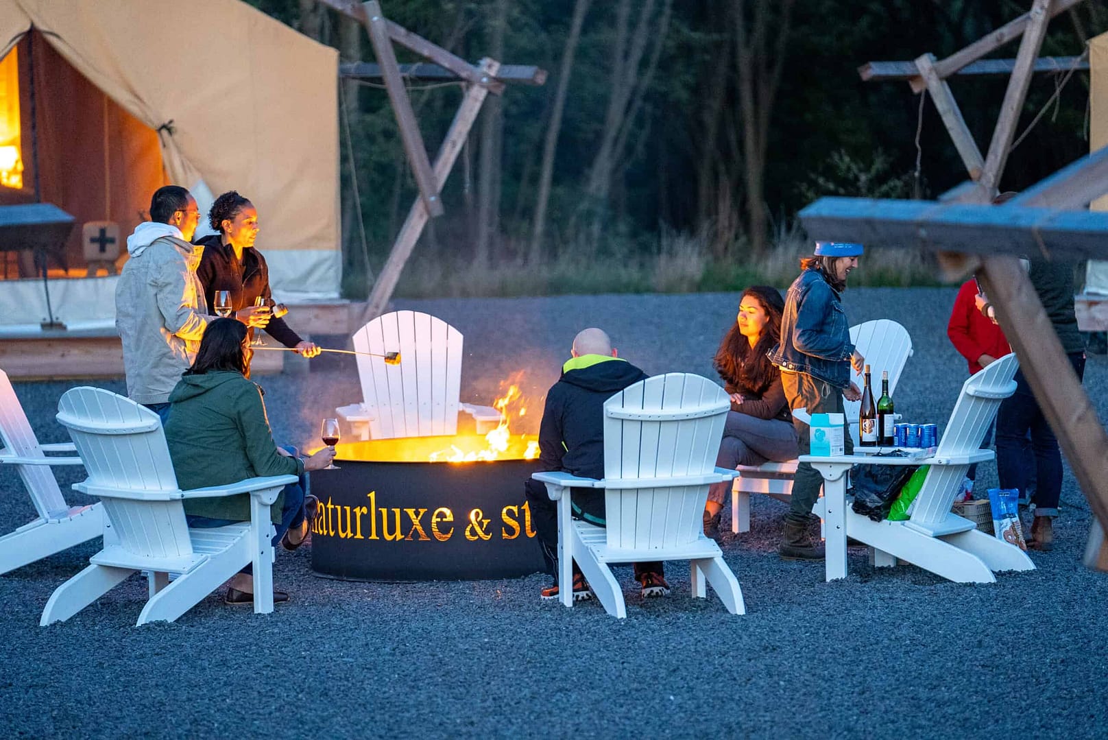 A group of people sitting around a fire pit in front of a tent.