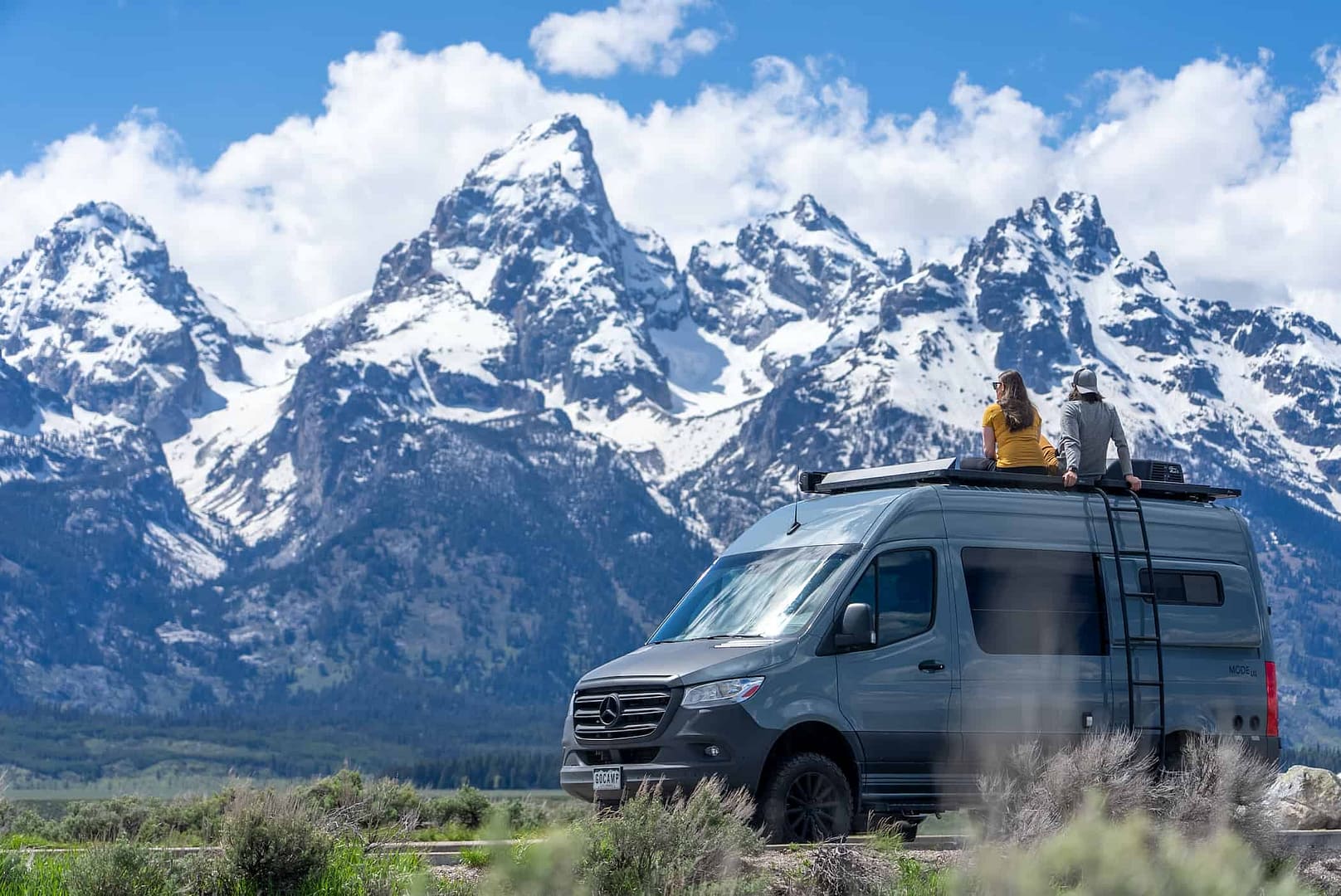 Two people standing on top of a GoCamp RV rental in front of the grand teton mountains.