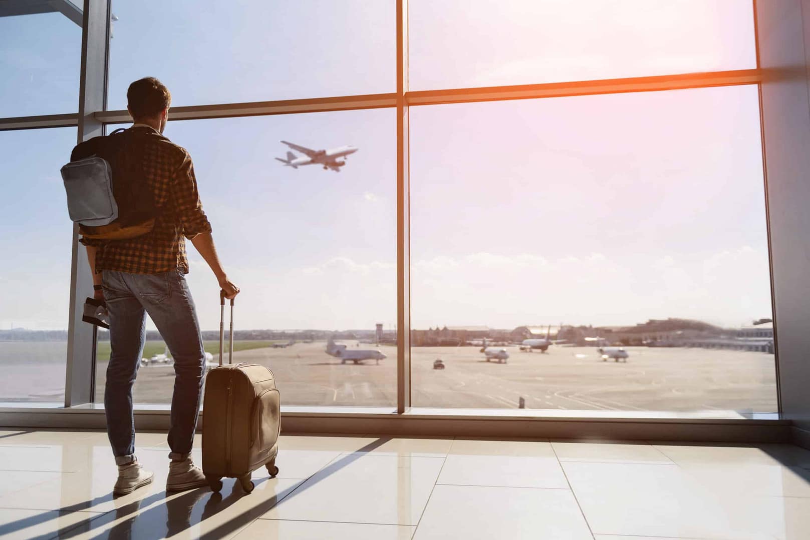 A man with a backpack looking out of an airport window at a US Airlines terminal, as he contemplates a turning point in his life's recovery journey.