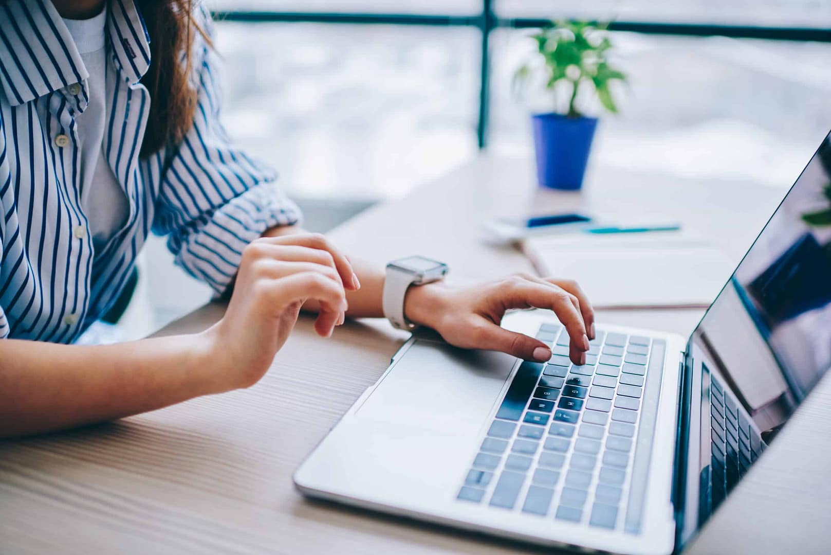 Woman in a striped shirt using a laptop at a desk, checking her smartwatch for short-term rental bookings.