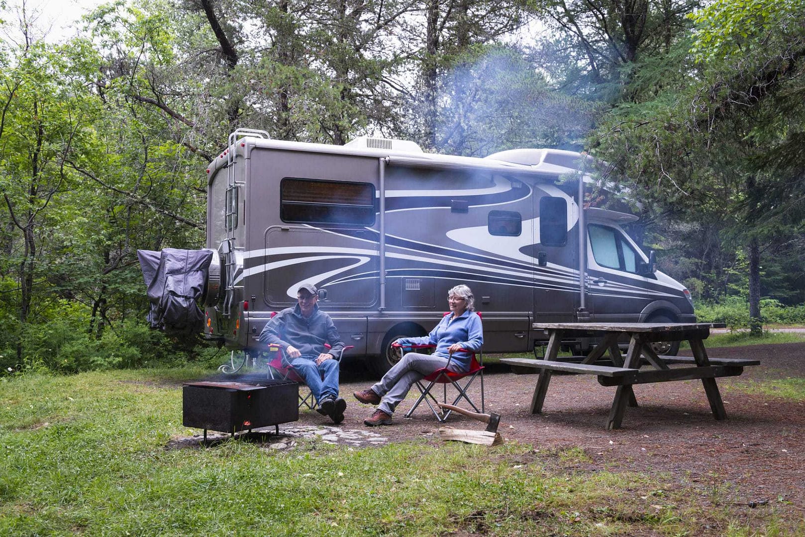 Two people sitting around a campfire in front of an RV, enjoying their time together.